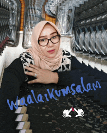 a woman wearing glasses and a hijab is sitting in front of a sign that says waalakum salam