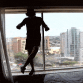 a man is jumping in the air in front of a window with a view of a city