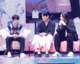 three men are sitting on a pink couch talking