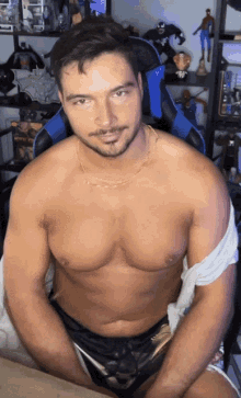 a shirtless man is sitting in front of a shelf with action figures
