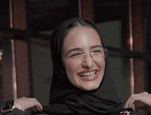 a woman wearing a hijab and glasses is smiling