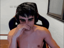 a shirtless man wearing headphones sits in a chair covering his nose