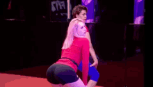 a woman in a red shirt and black shorts is dancing on a stage .