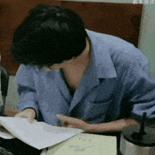 a man in a blue shirt is sitting at a desk looking at a piece of paper