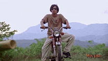 a man riding a motorcycle with mountains in the background and man laksa written on the bottom right