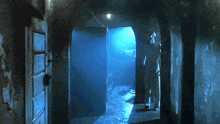 a man is standing in a dark hallway with a blue light shining through the doors