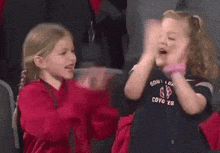 two little girls are clapping in a stadium wearing shirts that say coyotes