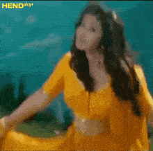 a woman in a yellow top is dancing in front of a blue sky with hendsky written on the bottom