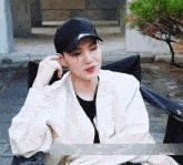 a young man wearing a baseball cap and a white jacket is sitting in a chair and crying .