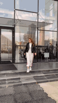 a woman in a black jacket and white pants is walking down stairs