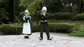 a man in a tuxedo and a woman in a maid outfit stand on a stone walkway