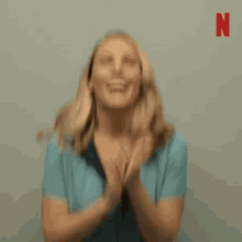 a woman in a blue dress is clapping her hands in front of her face .