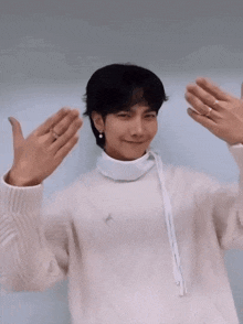 a young man wearing a white sweater and pearl earrings is making a funny face