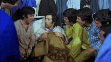 a group of men are sitting around a man in a bed