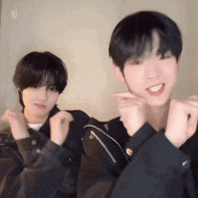 two young men are making a heart shape with their hands and smiling .