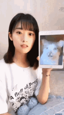a woman wearing a shirt that says " a fluff of poro " holds up a picture of a cat