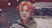 a young man with red hair is surrounded by confetti and looking at the camera .