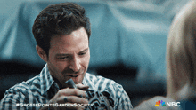 a man in a plaid shirt is talking to a woman with a nbc logo in the background