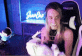 a woman wearing headphones is sitting in a gaming chair holding a stuffed animal and smiling .