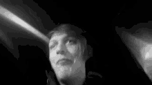a black and white photo of a person in a dark room looking up at the camera .