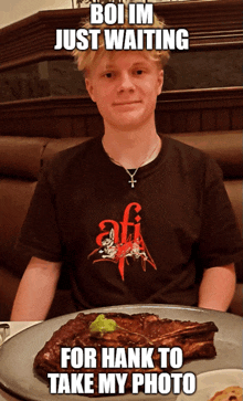 a young man is sitting at a table with a plate of food and a meme that says boi im just waiting for hank