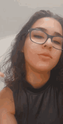 a woman wearing glasses and a black tank top looks at the camera