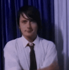 a man in a white shirt and tie is sitting in front of a blue curtain and smiling .