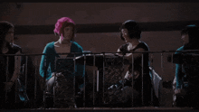 a woman with pink hair stands in front of a man 's face with an exit sign in the background