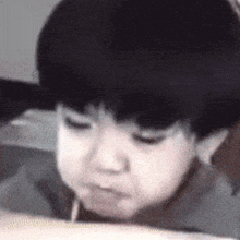 a young boy is drinking from a straw while sitting at a table .
