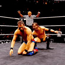 two men are wrestling in a wrestling ring with a referee in the background and a w logo on the ring
