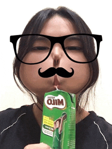 a woman wearing glasses and a fake mustache is drinking a carton of milo