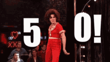 a man in a red jumpsuit is dancing in front of a crowd with the number 5 and 0 behind him