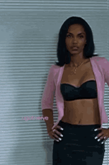 a woman wearing a black bra and a pink cardigan stands in front of blinds