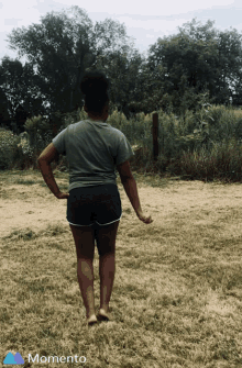 a woman in shorts and a t-shirt is walking barefoot in a field with the word momento on the bottom