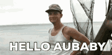 a man in a tank top is standing in the water with the words hello aubaby below him .