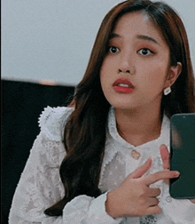 a woman in a white lace shirt is holding a cell phone and pointing at it