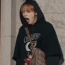 a woman is wearing a black hoodie and yawning while holding a bag .