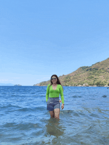 a woman in a green top and shorts is standing in the ocean