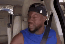 a man wearing a hat and a blue tank top is sitting in the back seat of a car
