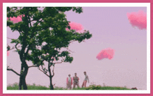 a group of people standing under a tree with pink clouds in the sky