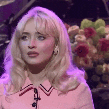 a blonde woman in a pink dress is standing in front of a piano and flowers .