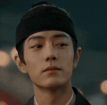 a close up of a young man wearing a black hat and looking at the camera .