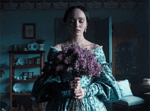 a woman in a blue dress holds purple flowers
