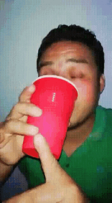 a man in a green shirt is drinking from a red plastic cup