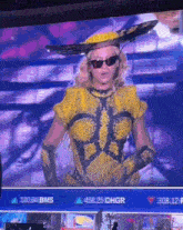 a woman in a yellow outfit is standing in front of a screen that says ' bms ' on it
