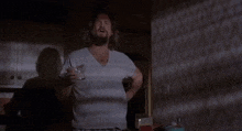 a man in a white shirt is holding a glass of water in a kitchen .