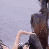 a woman with long black hair is standing in front of a purple background and holding her hair up in the air .