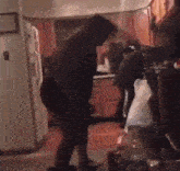 a couple of people are standing in a kitchen with a bag on the floor .