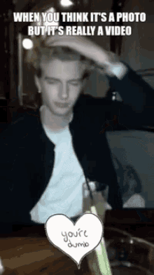a man is sitting at a table with a drink and a heart that says " you 're dumb "