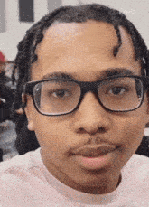 a close up of a young man wearing glasses and braids .